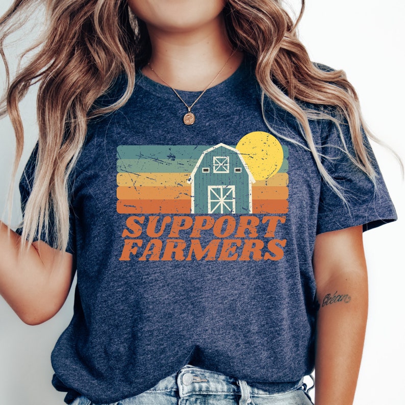 May include: A navy blue t-shirt with a vintage-style graphic of a barn, sun, and the text "SUPPORT FARMERS".