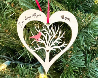 May include: White wooden heart-shaped ornament with a cutout tree and a red bird. The ornament has the text "I am always with you" and "Mom" written on it.