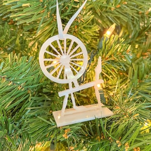 May include: White spinning wheel Christmas ornament hanging on a green artificial Christmas tree.