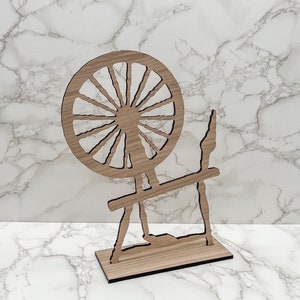 May include: Wooden spinning wheel cutout, a decorative piece with a large wheel and a stand. The wheel has a sunburst design with spokes radiating from the center.