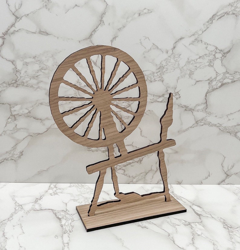 May include: Wooden spinning wheel cutout, a decorative piece with a large wheel and a stand. The wheel has a sunburst design with spokes radiating from the center.