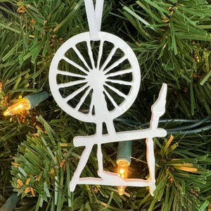 May include: White spinning wheel Christmas ornament hanging on a green artificial Christmas tree with white lights.