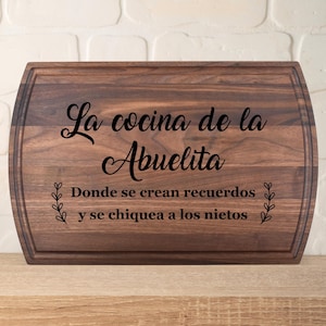 Peut inclure: Planche à découper rectangulaire en bois brun foncé. Le texte "La cocina de la Abuelita" et "Donde se crean recuerdos y se chiquea a los nietos" est gravé en noir sur la planche.