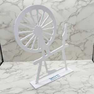 May include: White wooden spinning wheel cutout with a base that reads "Laura's New" and "January 25, 2023".