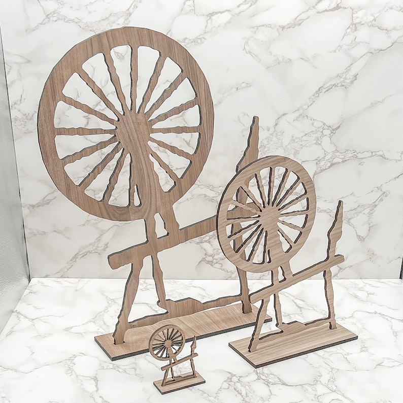 May include: Three wooden spinning wheels of different sizes. The largest wheel is in the background and the smallest wheel is in the foreground. All three wheels are made of wood and have a simple design.