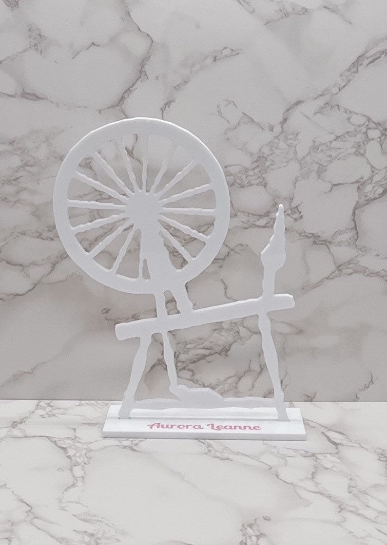 May include: White wooden spinning wheel cutout with the name "Aurora Leanne" written on the base.