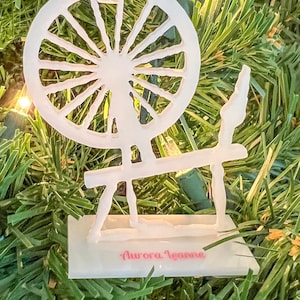 May include: White spinning wheel Christmas ornament with the text "Aurora Jeanne" on the base.