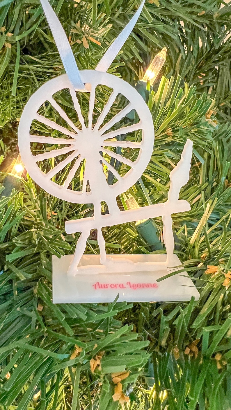 May include: White spinning wheel Christmas ornament with the text "Aurora Jeanne" on the base.