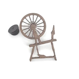 May include: A wooden spinning wheel and a black bottle stopper are displayed against a white background. The spinning wheel is brown with a circular wheel design and a detailed frame. The bottle stopper is dark gray.