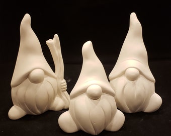 May include: Three white ceramic gnomes, each with a pointed hat and a beard. The gnome on the left is holding a stick in its hand.