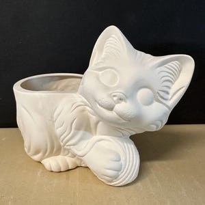 May include: White ceramic planter shaped like a cat curled up with its paws tucked under its chin. The planter has a wide opening for planting.