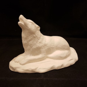 Puede incluir: Escultura de cerámica blanca de un lobo aullando a la luna. El lobo está acostado sobre una base rocosa.