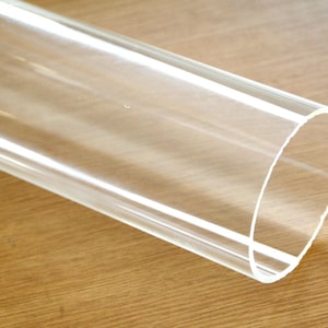 Puede incluir: Un tubo de acrílico transparente con una superficie lisa y pulida. El tubo es cilíndrico y tiene un diámetro de aproximadamente 7,6 cm.