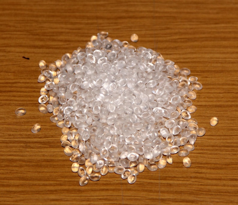 K&ouml;nnte beinhalten: Nahaufnahme eines Haufens transparenter Plastikperlen. Die Perlen sind klein und rund und liegen auf einer Holzoberfl&auml;che.