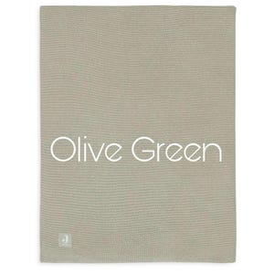 Puede incluir: Manta de punto verde oliva. La manta es de color liso con un aspecto texturizado. Las palabras "Olive Green" est&aacute;n escritas en blanco en la manta. Una peque&ntilde;a etiqueta con una "J" est&aacute; en la esquina inferior izquierda.