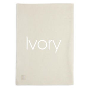 Puede incluir: Manta rectangular de color marfil con una superficie texturizada. La palabra "Ivory" est&aacute; impresa en blanco en el centro de la manta. Una peque&ntilde;a etiqueta cuadrada est&aacute; en la esquina inferior.