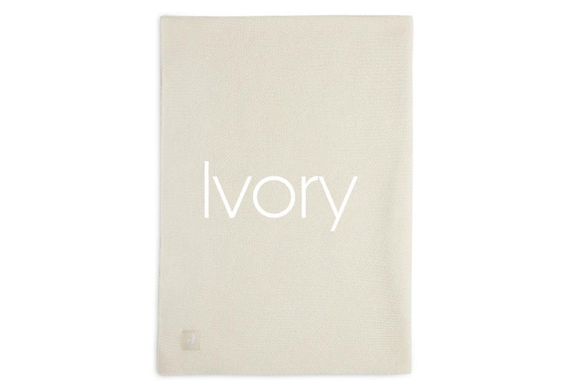 Puede incluir: Manta rectangular de color marfil con una superficie texturizada. La palabra "Ivory" est&aacute; impresa en blanco en el centro de la manta. Una peque&ntilde;a etiqueta cuadrada est&aacute; en la esquina inferior.