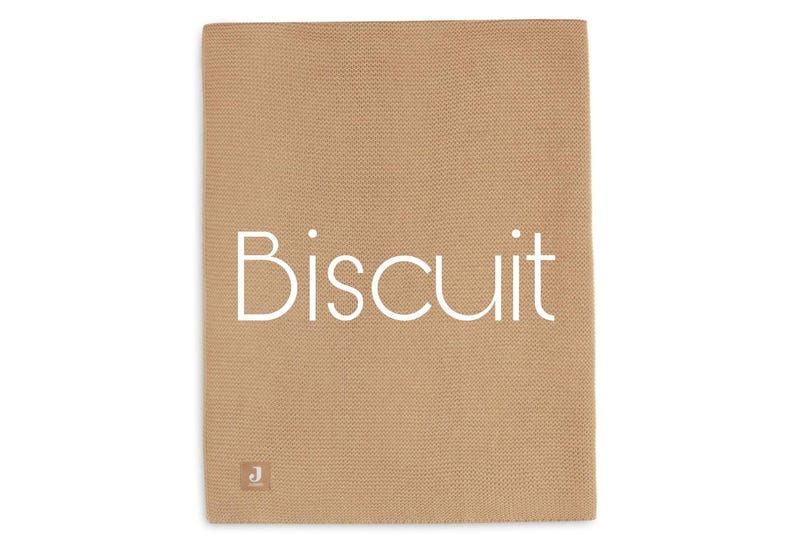 Puede incluir: Una manta de punto de color beige con la palabra "Biscuit" en blanco, centrada en la parte delantera. La manta tiene un aspecto texturizado y una peque&ntilde;a etiqueta en la esquina inferior izquierda.