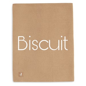Puede incluir: Una manta de punto de color beige con la palabra "Biscuit" en blanco. La manta tiene un aspecto texturizado y una peque&ntilde;a etiqueta en la esquina inferior izquierda.