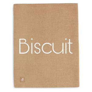 Puede incluir: Una manta de punto de color beige con la palabra "Biscuit" en blanco, centrada en la parte delantera. La manta tiene un aspecto texturizado y una peque&ntilde;a etiqueta en la esquina inferior izquierda.