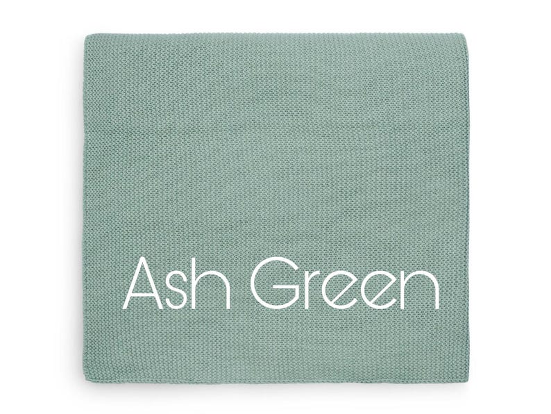 Puede incluir: Un textil plegado de color verde ceniza apagado, con una textura tejida visible. Las palabras "Ash Green" est&aacute;n impresas en blanco en el centro. El textil es de forma cuadrada.