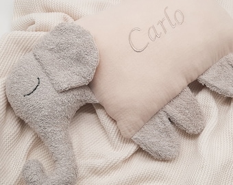Peut inclure: Un coussin en forme d'éléphant en tissu texturé gris clair avec une section centrale rectangulaire beige douce brodée du nom Carlo en écriture cursive, posé sur une surface en tissu tricoté de couleur crème.
