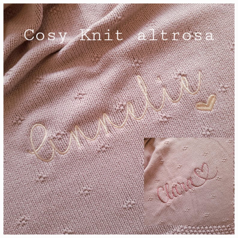 Puede incluir: Una manta de punto suave, de color rosa empolvado, con un nombre bordado en cursiva. La manta tiene un patr&oacute;n texturizado con peque&ntilde;os puntos en relieve. Las palabras "Cosy Knit altrosa" est&aacute;n en la parte superior.