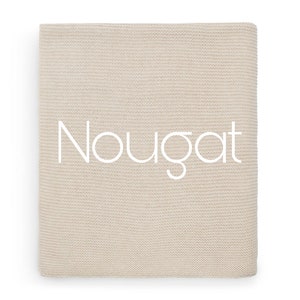 Puede incluir: Una manta tejida beige doblada con la palabra "Nougat" en escritura blanca en la parte delantera. La manta tiene un aspecto texturizado y probablemente est&aacute; hecha de un material suave.