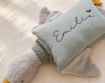 Op de afbeelding: Een pluche gansvormig kussen met een zacht grijs getextureerd lichaam, een gele snavel en een lichtgroen rechthoekig middengedeelte. Het groene gedeelte bevat de geborduurde naam Emilia in donkergroen schrift met een klein hartje.