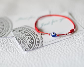 May include: Red string bracelet with a blue evil eye charm and silver beads. The bracelet is on a white card with the text "Just for you" and "www.justseedbeads.etsy.com".