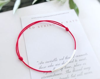 May include: Red string bracelet with a silver bar charm. The bracelet is on a white card with the text "Red String of Fate" and a quote about the meaning of the red string.