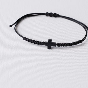 May include: A black braided cord bracelet with a black cross charm.