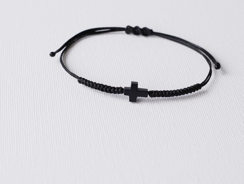 May include: A black braided cord bracelet with a black cross charm.