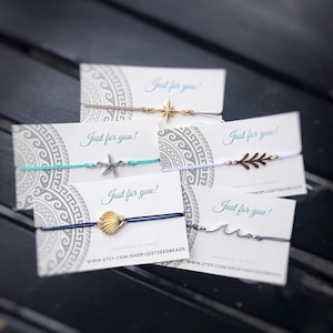 Könnte beinhalten: Fünf Karten mit dem Text "Just for you!" und verschiedenen Charms, darunter ein Stern, ein Seestern, eine Muschel, ein Zweig und eine Welle. Die Karten sind mit einem grau-weißen Muster verziert.