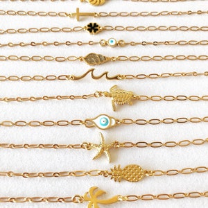Könnte beinhalten: Ein Set aus neun goldenen Kettenarmbändern mit verschiedenen Anhängern, darunter eine Ananas, eine Palme, ein Seestern, ein böses Auge, eine Schildkröte, eine Welle, ein Blatt, ein Kreuz und ein Blatt.
