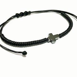 May include: A black braided cord bracelet with a silver cross charm.