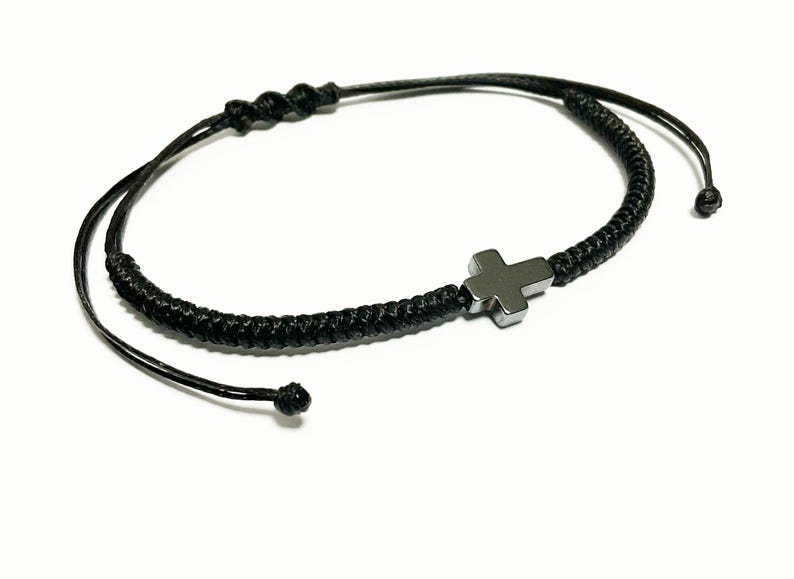 May include: A black braided cord bracelet with a silver cross charm.