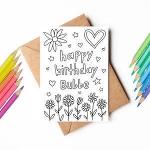 May include: A black and white coloring card with the words "happy birthday Bubbe" surrounded by floral and heart designs. The card is on a brown envelope with colored pencils in the background.