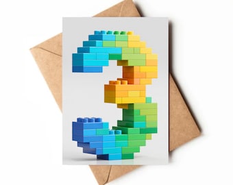 Puede incluir: Una tarjeta de felicitación con el número "3" construido con bloques de construcción de colores. El número hace una transición de azul a verde, amarillo y naranja. La tarjeta está sobre un fondo blanco, con un sobre marrón parcialmente visible.
