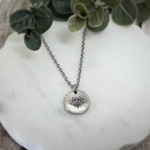 May include: A silver chain necklace with a round pendant featuring a detailed lotus flower design.
