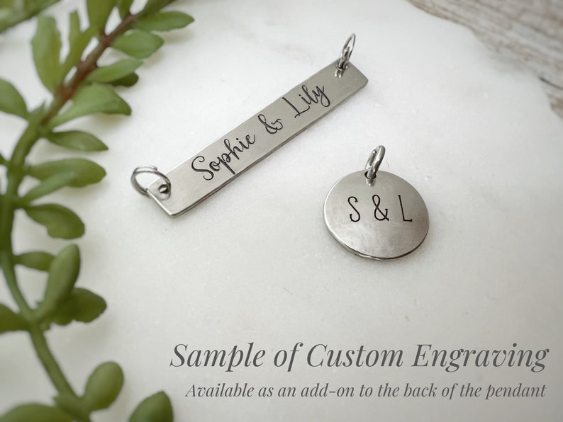 May include: A silver-toned rectangular bar pendant engraved with the text Sophie & Lily and a circular pendant engraved with the letters S & L. Both metal charms feature small jump rings attached to the top for hanging on a necklace chain.