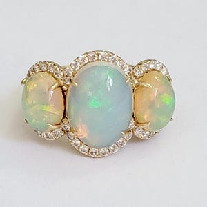 May include: A gold ring with three oval-shaped opals set in a halo of diamonds.
