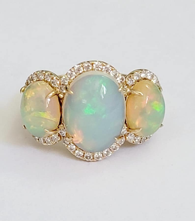 May include: A gold ring with three oval-shaped opals set in a halo of diamonds.