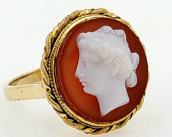 May include: A gold ring with a cameo set in a red carnelian stone. The cameo features a white profile of a woman with her hair pulled back.