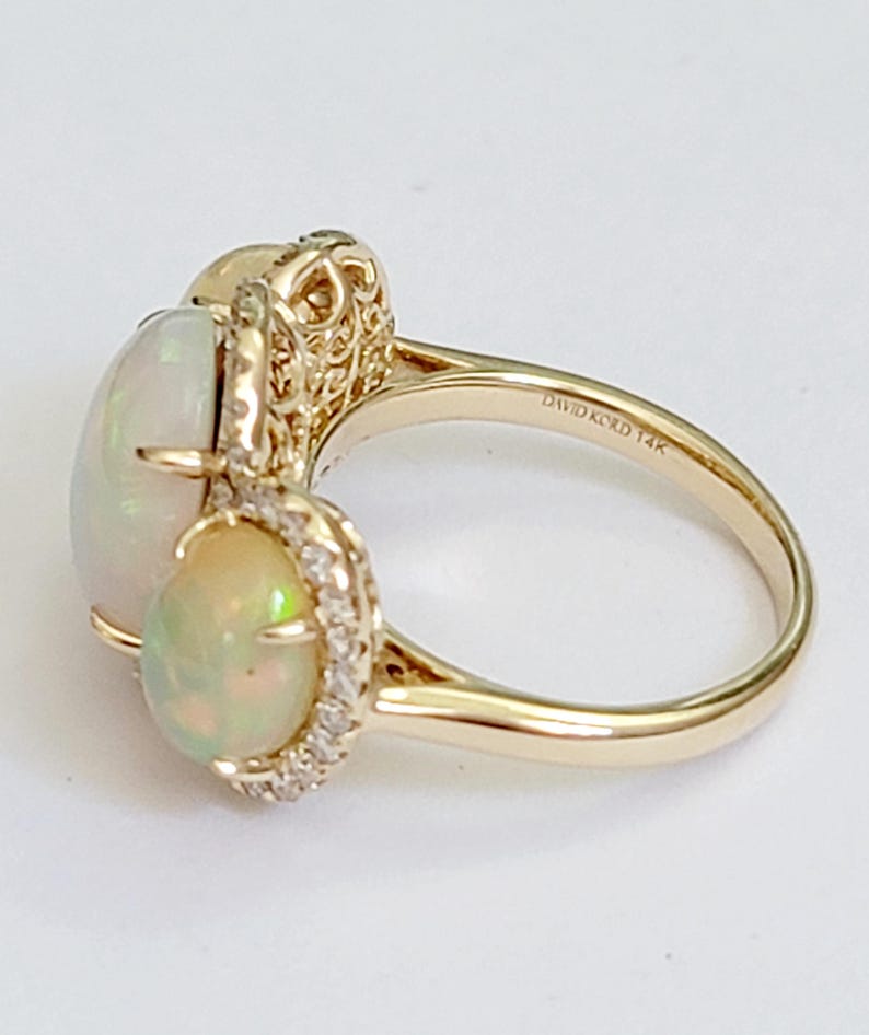 May include: A gold ring with two opal gemstones and a diamond halo setting. The ring is marked "DAVID KORD 14K" on the inside band.