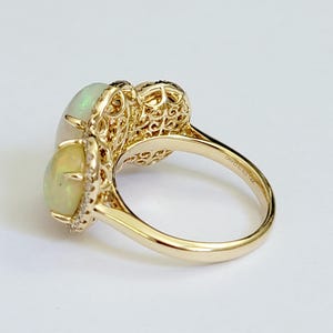 May include: A gold ring with two white opal stones and a filigree design. The ring is set with small diamonds around the opals.