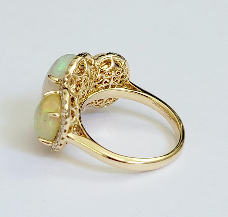May include: A gold ring with two white opal stones and a filigree design. The ring is set with small diamonds around the opals.