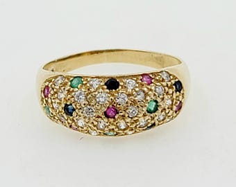 Può includere: Un anello con fascia in oro con una parte superiore larga e bombata incastonata con un gruppo di piccole pietre preziose colorate. L'anello è incastonato con diamanti, smeraldi, rubini e zaffiri.
