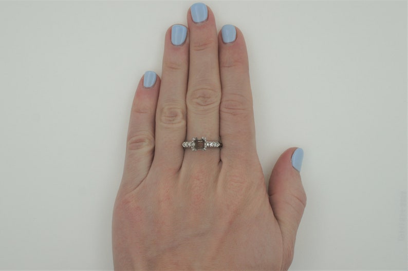 Puede incluir: Un anillo de plata con un engaste cuadrado para una piedra preciosa. El anillo tiene peque&ntilde;os diamantes en la banda.