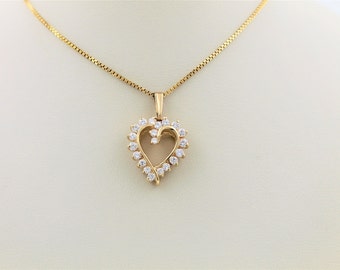 Puede incluir: Un collar de cadena de oro con un colgante en forma de corazón. El colgante está hecho de oro y tiene un diseño delicado con pequeñas piedras transparentes alrededor del borde.
